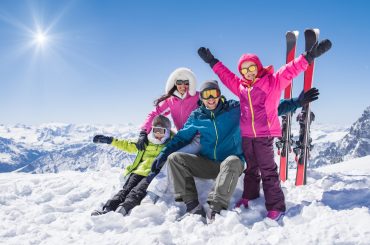 Laughing family in winter vacation with ski sport on snowy mountains. Happy man and woman with sons having fun and looking at camera. Family with two children enjoying winter holiday at ski resort.